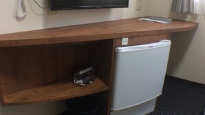 A hotel room with a flat-screen TV mounted on a wooden desk, a white telephone, and a small white refrigerator. - @ Business Hotel Ichinoseki (Ichinoseki)