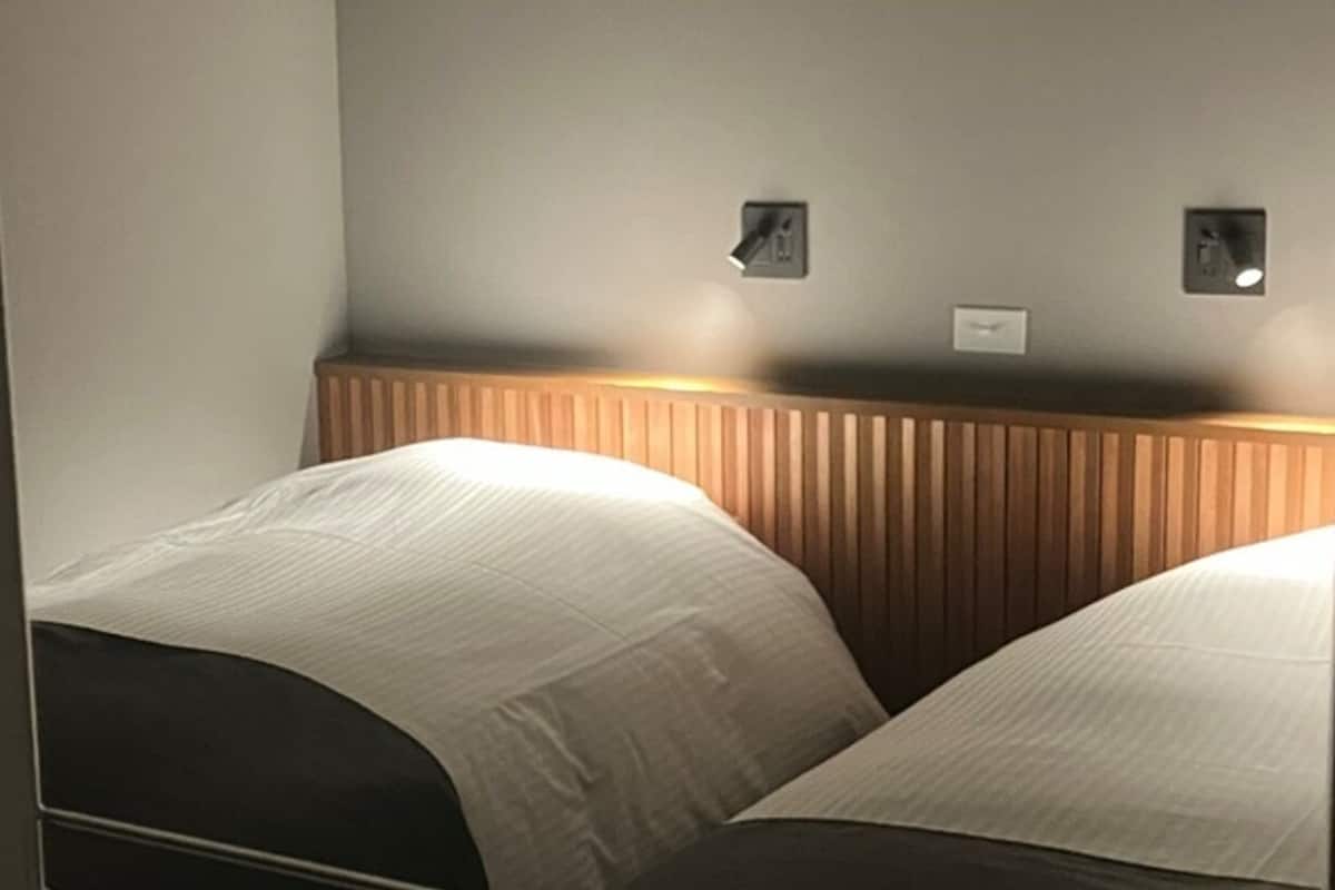 A hotel room with two beds, a wooden headboard, and two wall-mounted light switches.