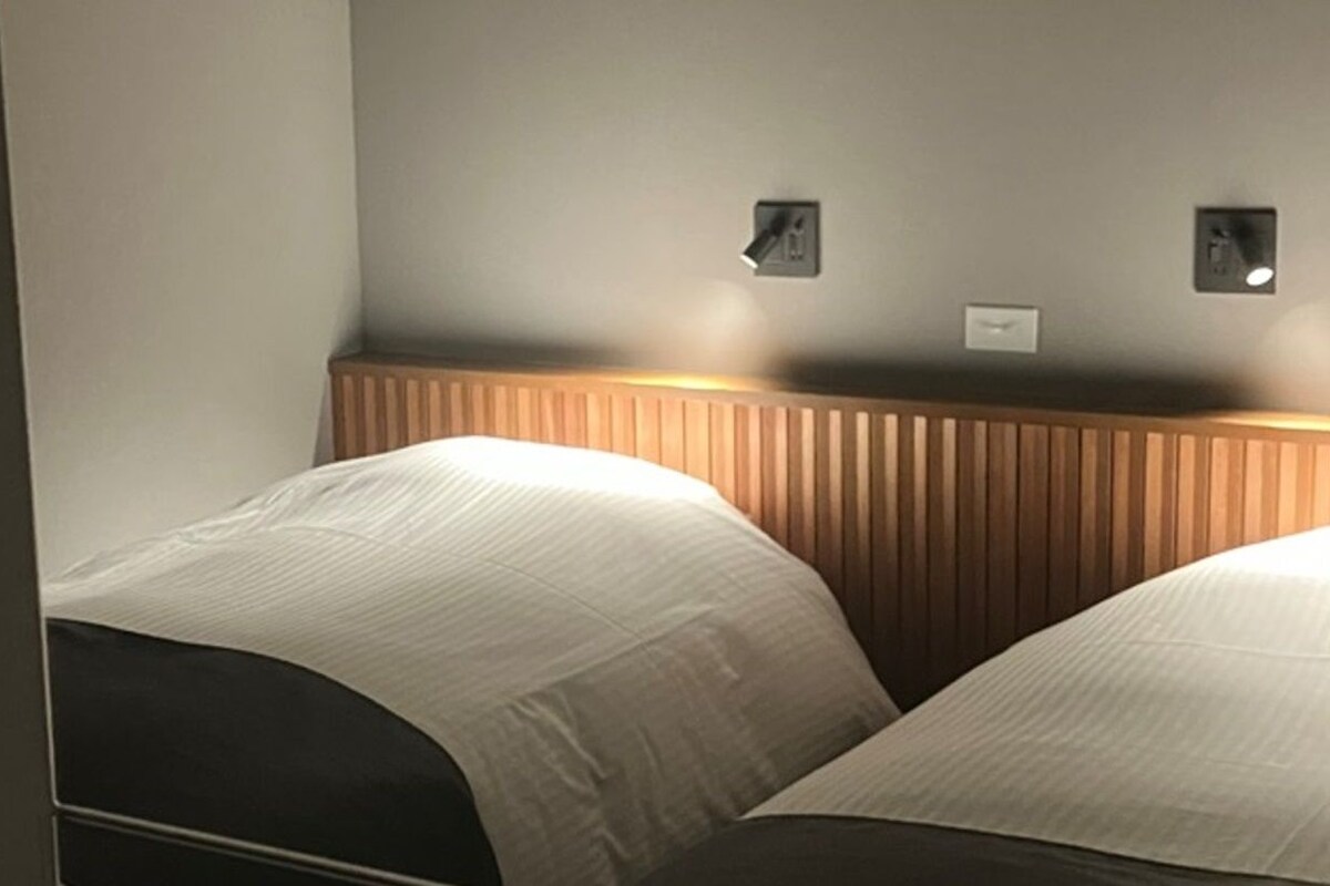 A hotel room with two beds, a wooden headboard, and two wall-mounted light switches.