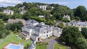 A large, multi-story residential building with a swimming pool, surrounded by lush greenery and other houses. - Lincombe Hall Hotel & Spa - Just for Adults (Torquay)