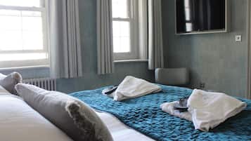 A hotel room with a bed, a TV mounted on the wall, and a window with curtains.