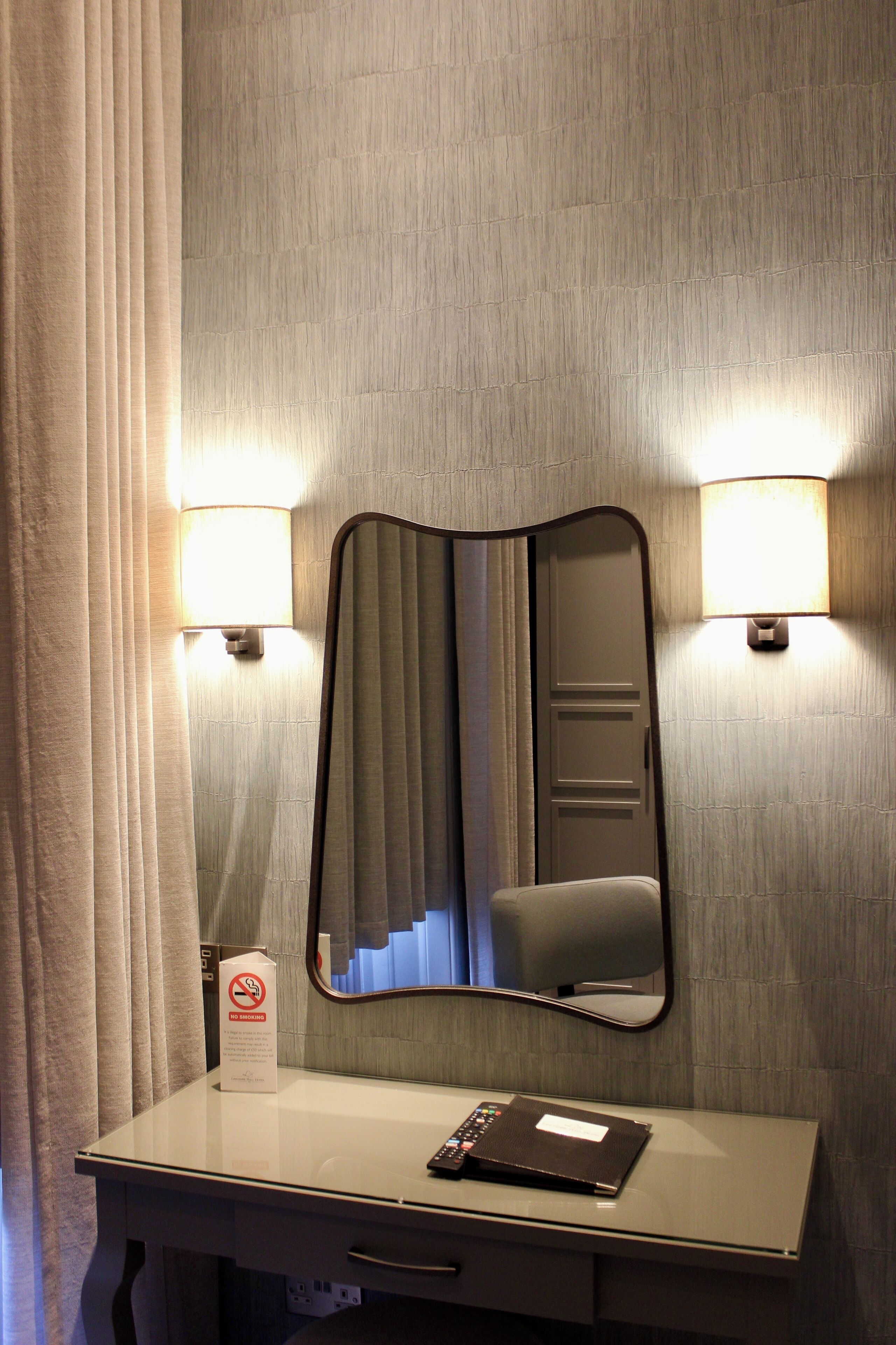 Une chambre d’hôtel équipée d’un miroir, d’un bureau et de deux lampes fixées au mur.