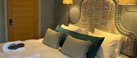 A neatly made bed with white linens and two towels, a wooden door, and a headboard with a patterned design.