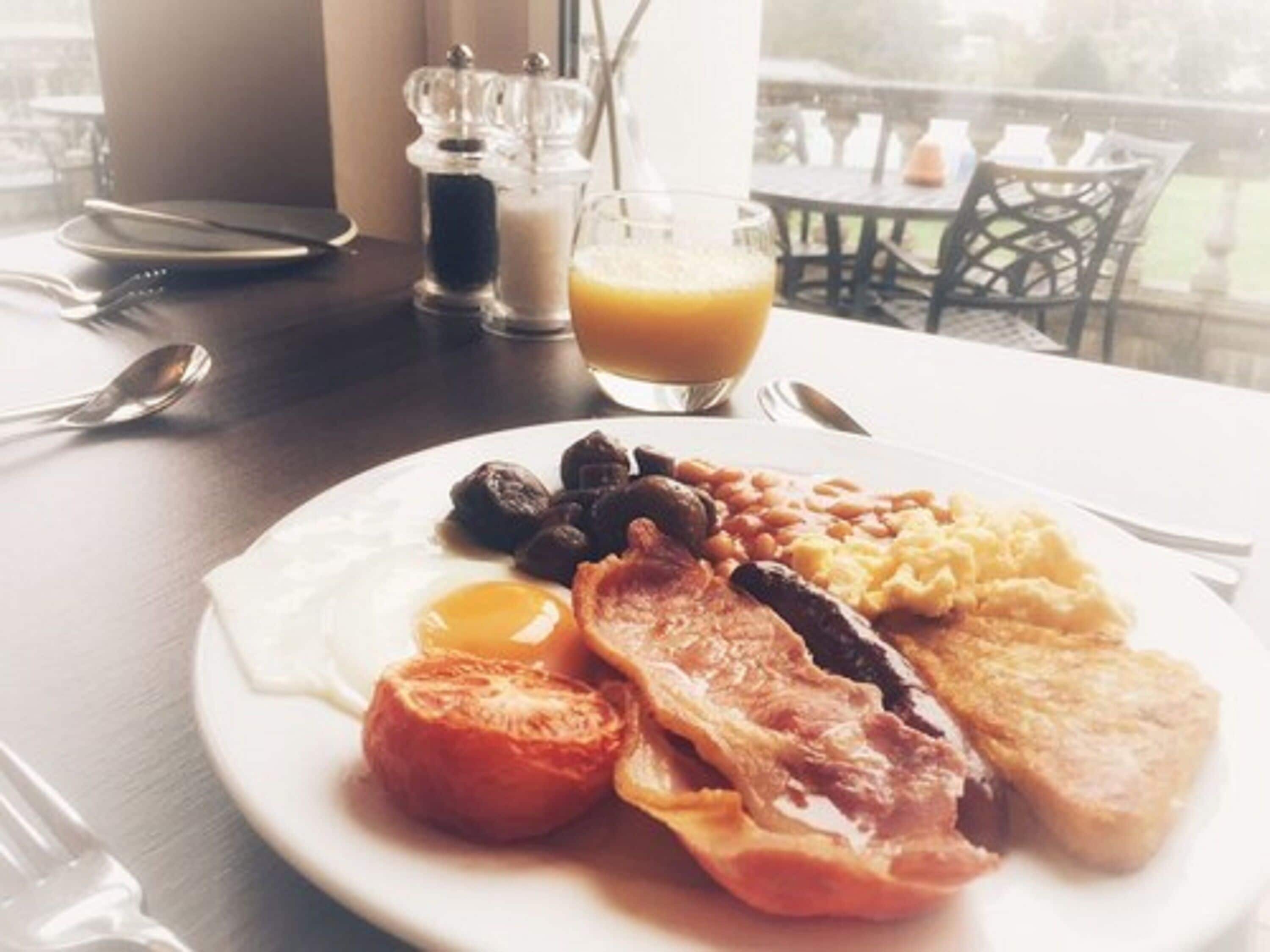 A breakfast plate with eggs, bacon, beans, tomatoes, and toast on a table with a glass of orange juice and salt and pepper shakers.
