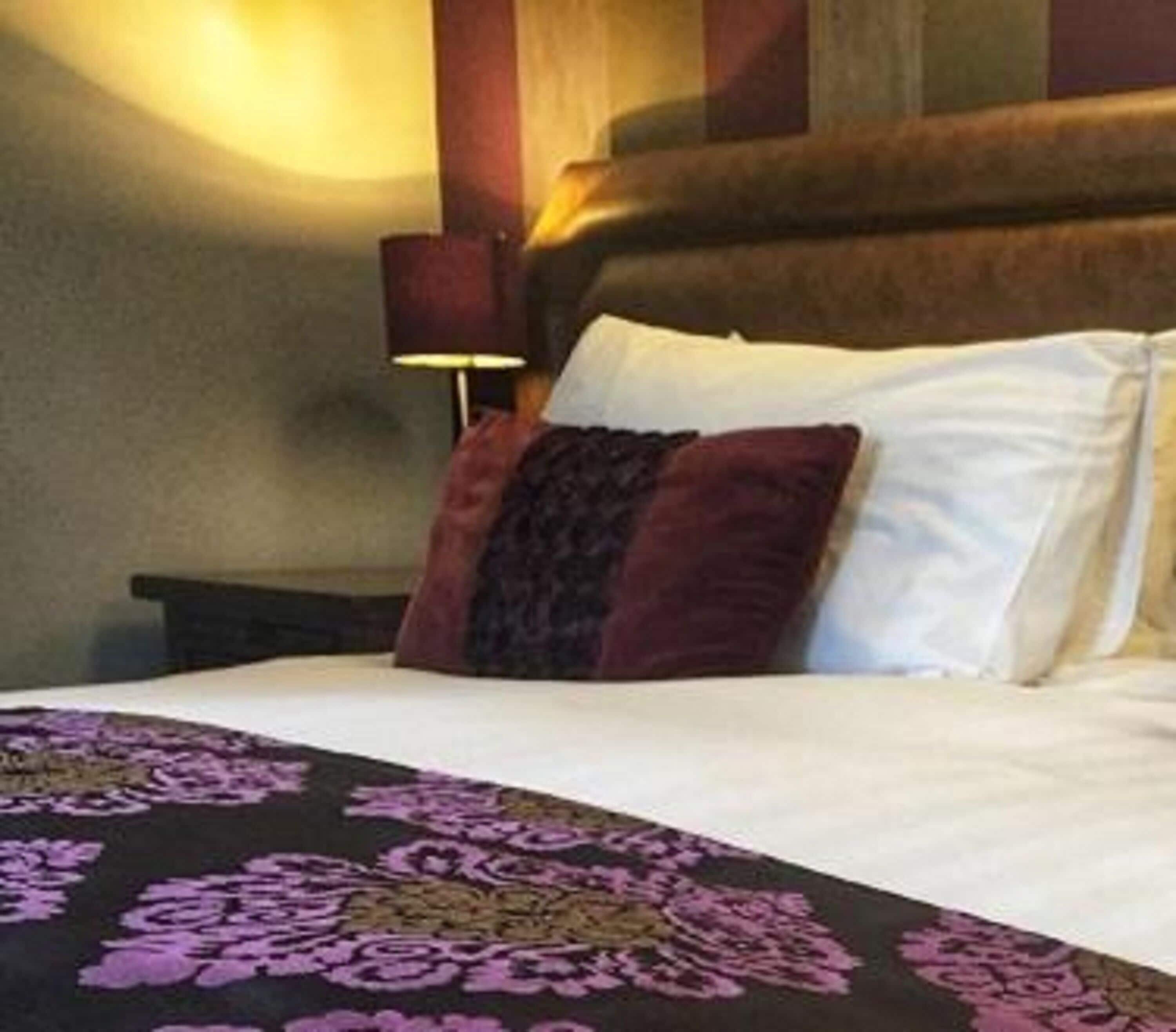 A hotel room with a bed, a nightstand, and a wall-mounted lamp.