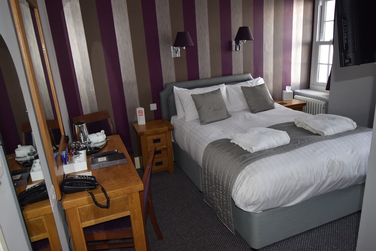A hotel room with a bed, bedside tables, a desk with a telephone, and a mirror.