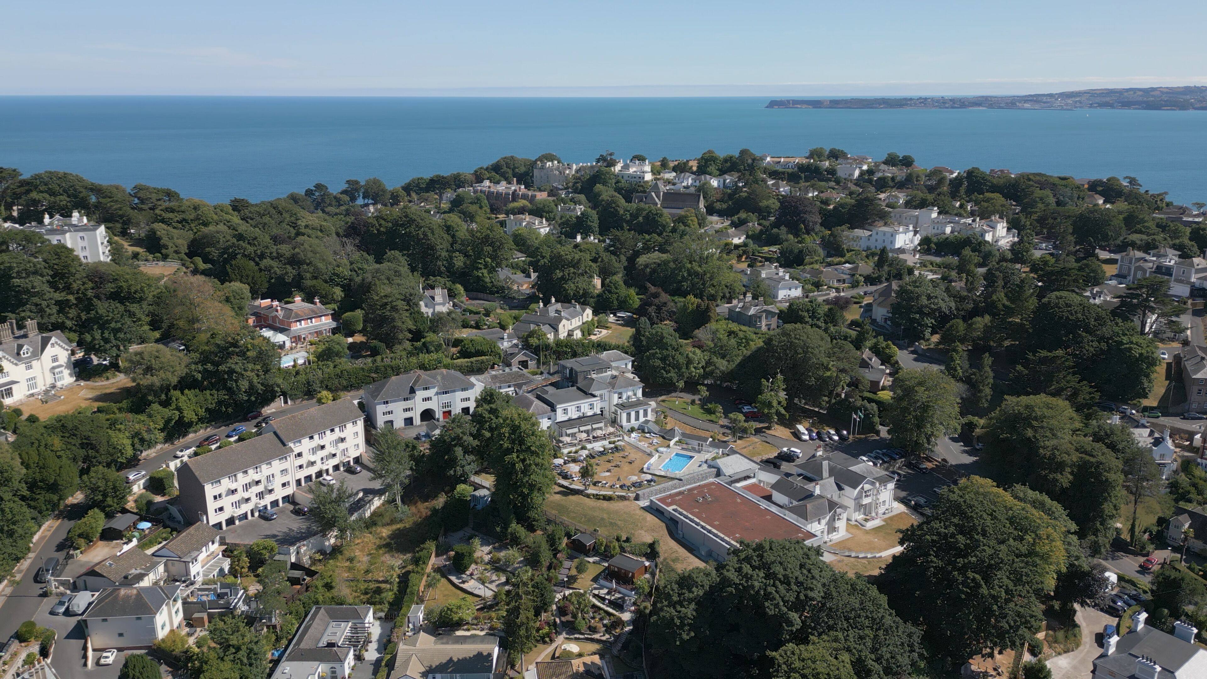Ett flygbildsbild av ett bostadsområde vid kusten med hus, en swimmingpool och en stor egendom med flera byggnader.