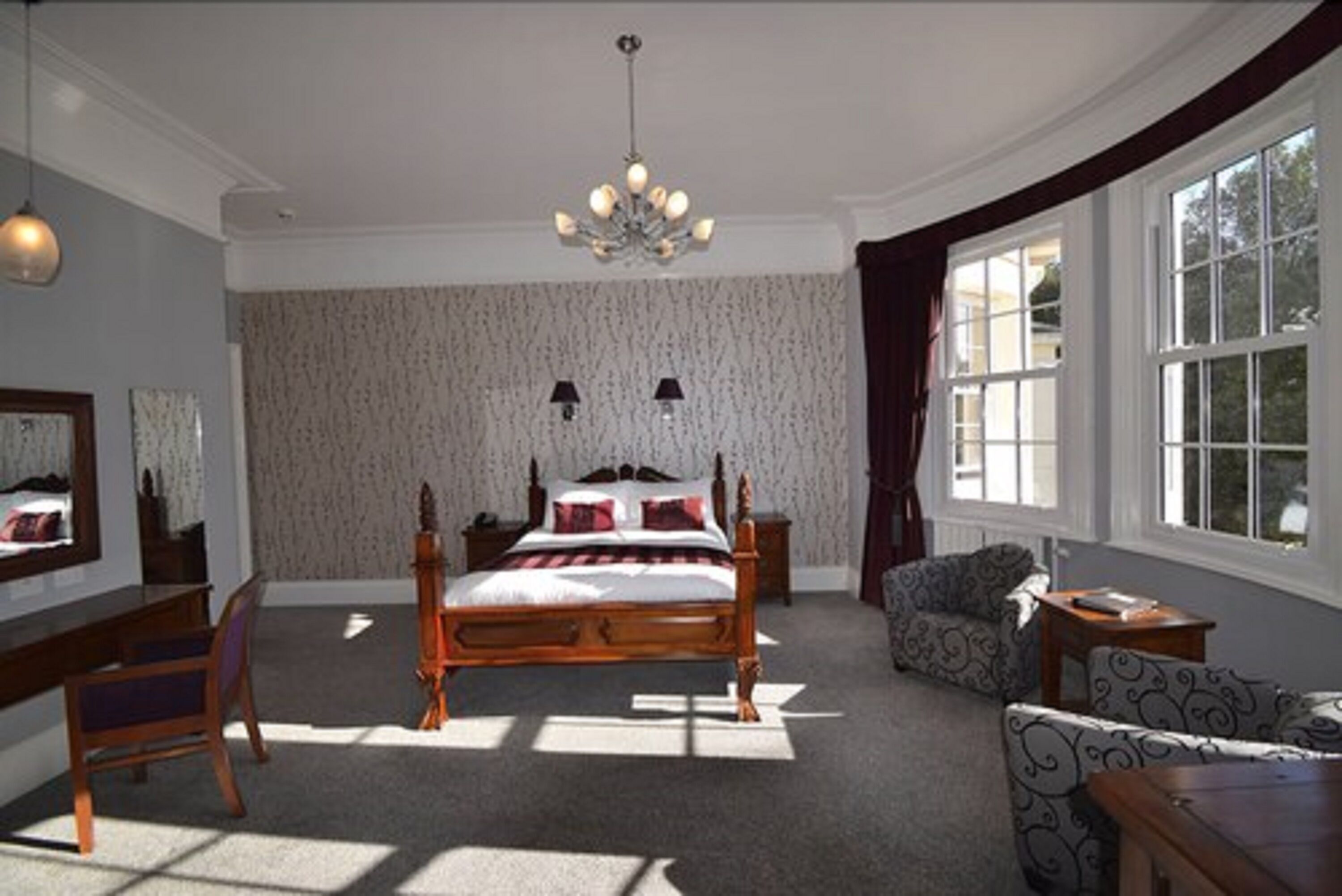 A bedroom with a large bed, a chandelier, a desk, and a window with curtains.