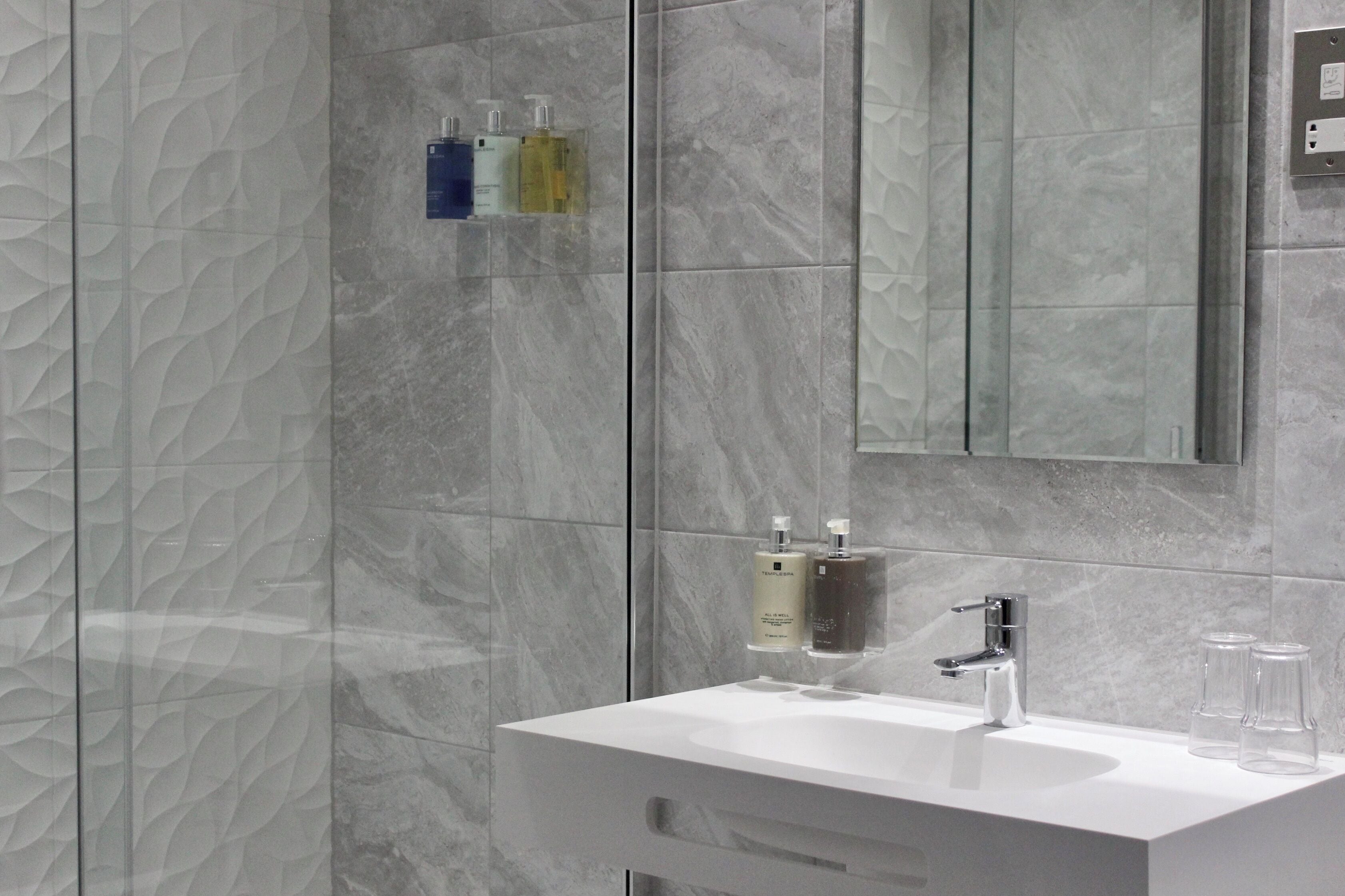 A modern bathroom with a white sink, a mirror, and marble-patterned walls.