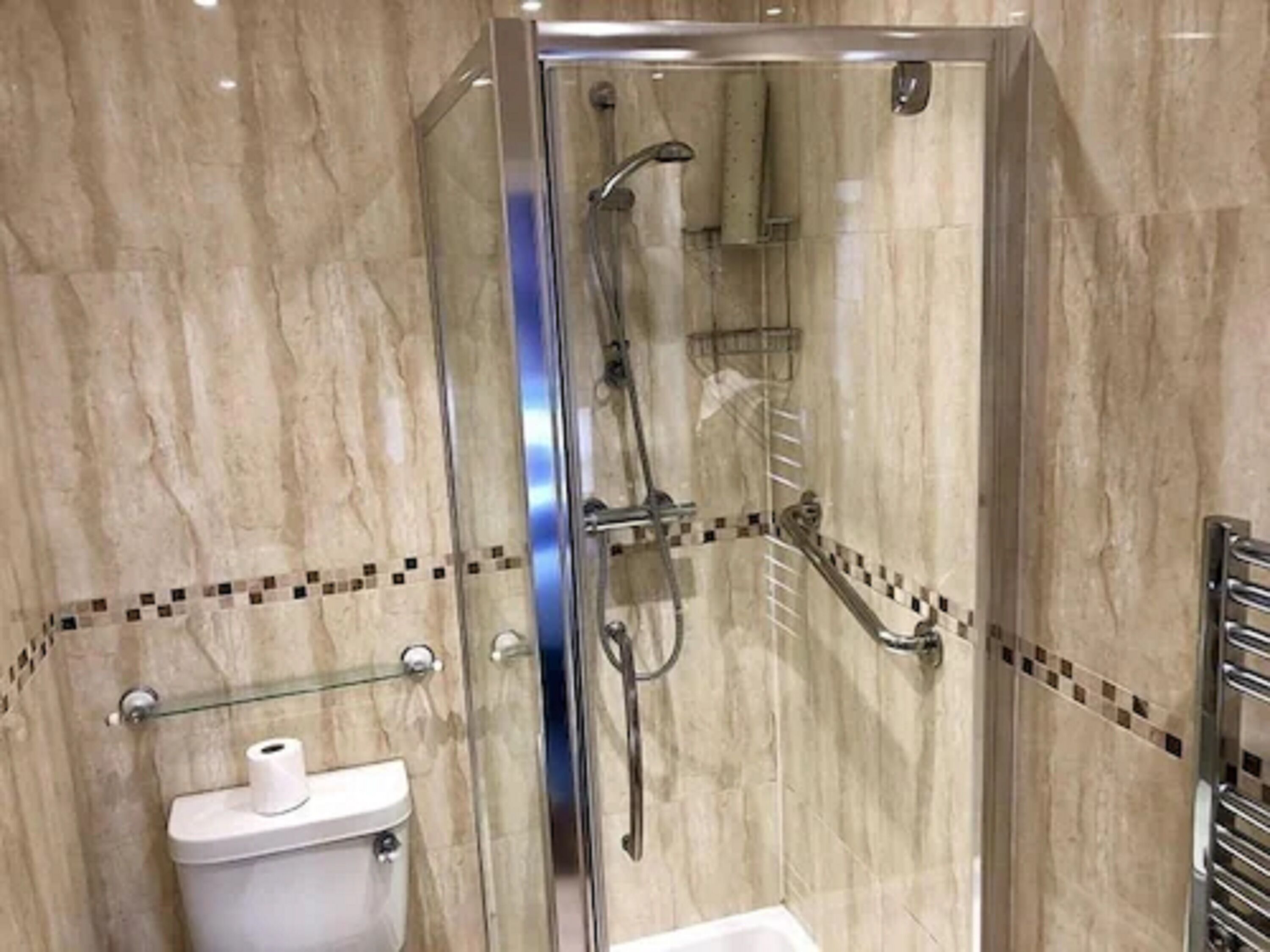 A glass-enclosed shower stall with a handheld showerhead and a wall-mounted towel rack.