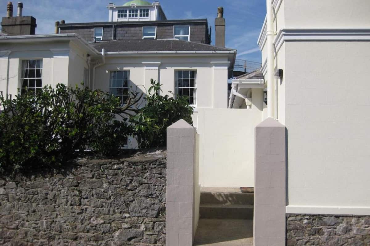 A white building with a stone wall and a small garden area.