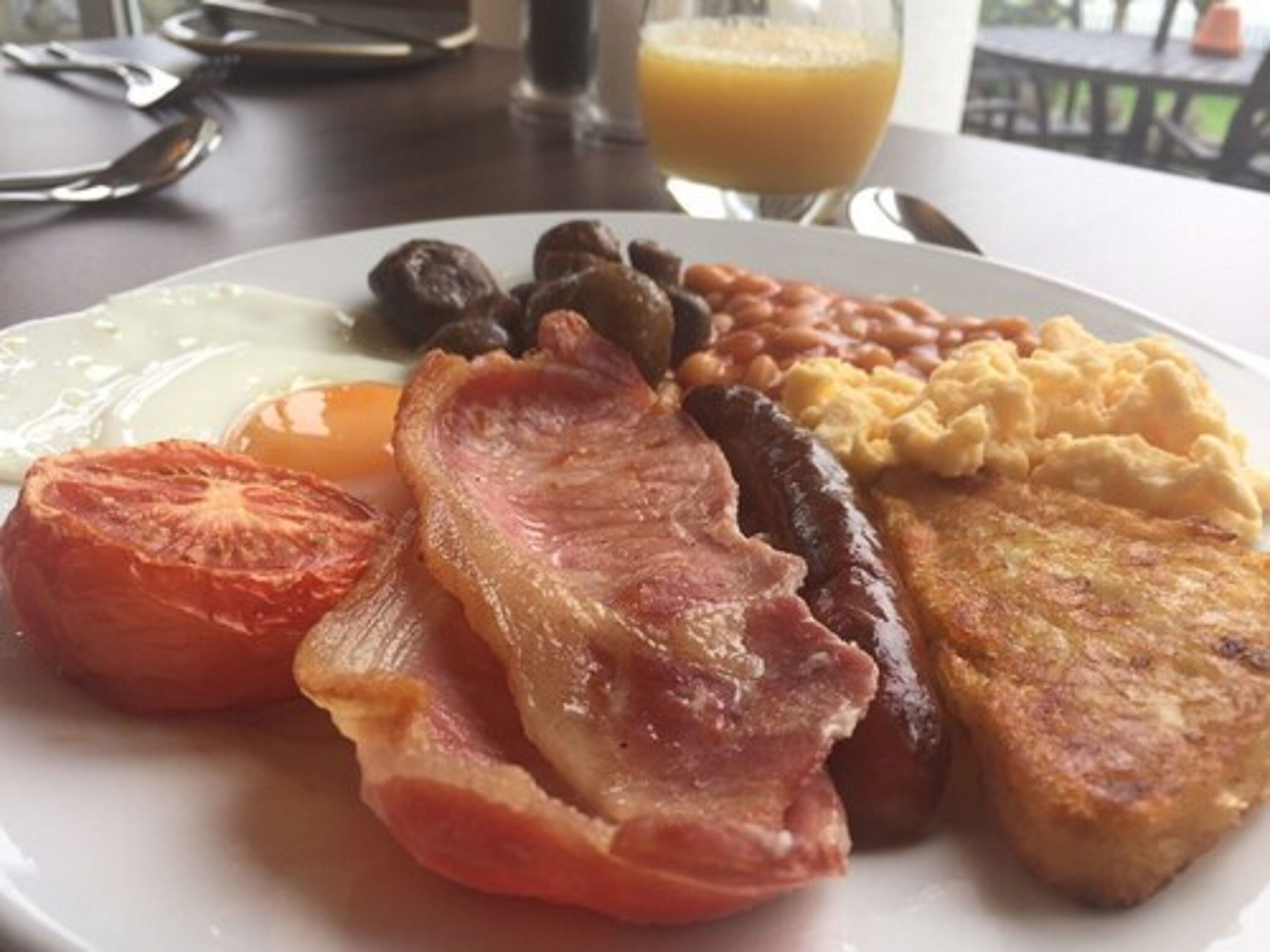 A breakfast plate with bacon, eggs, sausages, beans, toast, and a tomato.
