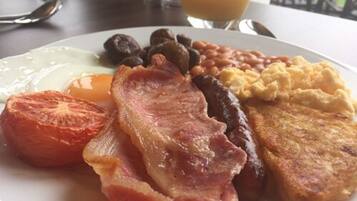 A breakfast plate with bacon, eggs, sausages, beans, toast, and a tomato.