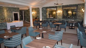 A restaurant with multiple tables and chairs, a bar area, and a large mirror on the wall.
