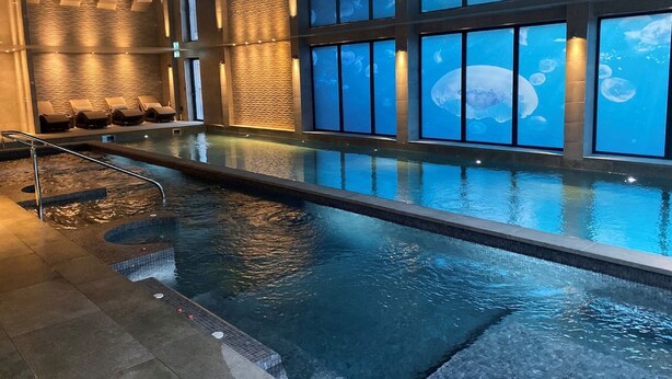 A swimming pool with a view of the night sky through large windows, a seating area with lounge chairs, and a textured wall. - Lincombe Hall Hotel & Spa - Just for Adults (Torquay)