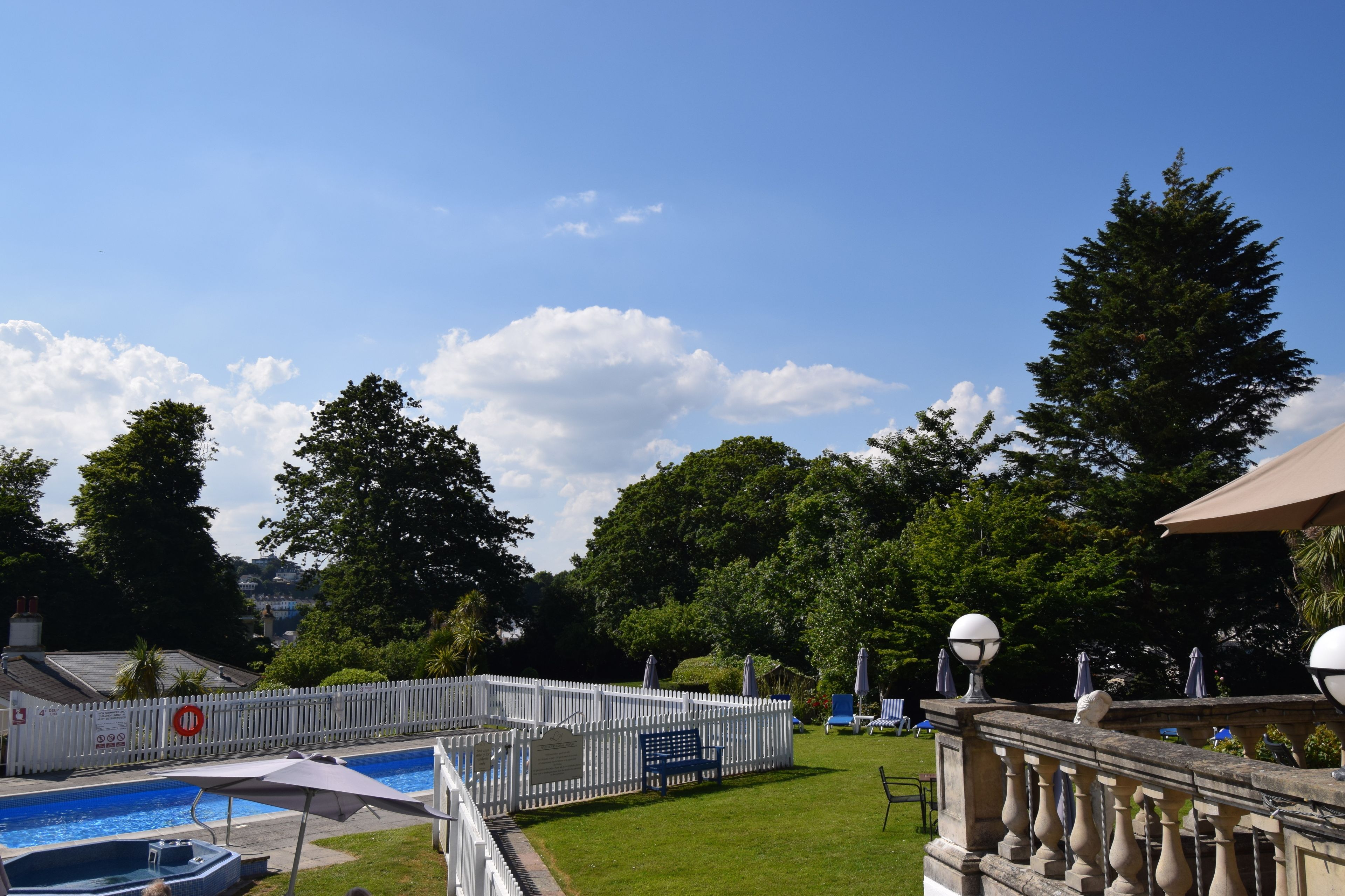 A swimming pool with a white fence, a bench, and umbrellas.