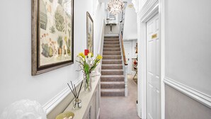 A hallway with a staircase, framed botanical artwork, a vase with flowers, and a private door. - Sandway House (Torquay)