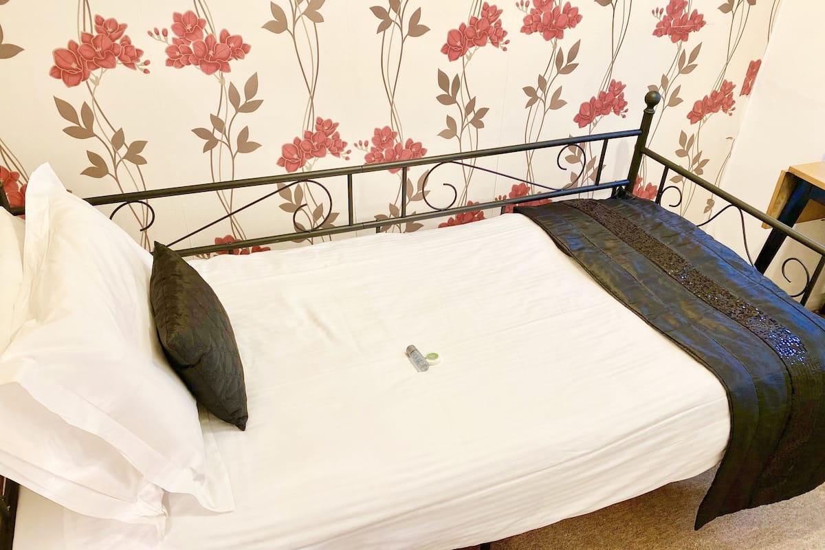 A neatly made bed with white linens, a dark green throw, and a single decorative pillow.