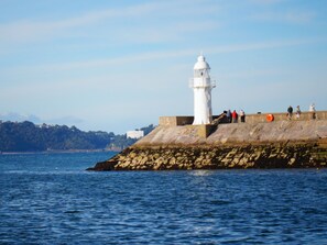 A lighthouse on a rocky outcrop with a clear view of the sea and distant hills. - The Trouville (Torquay)