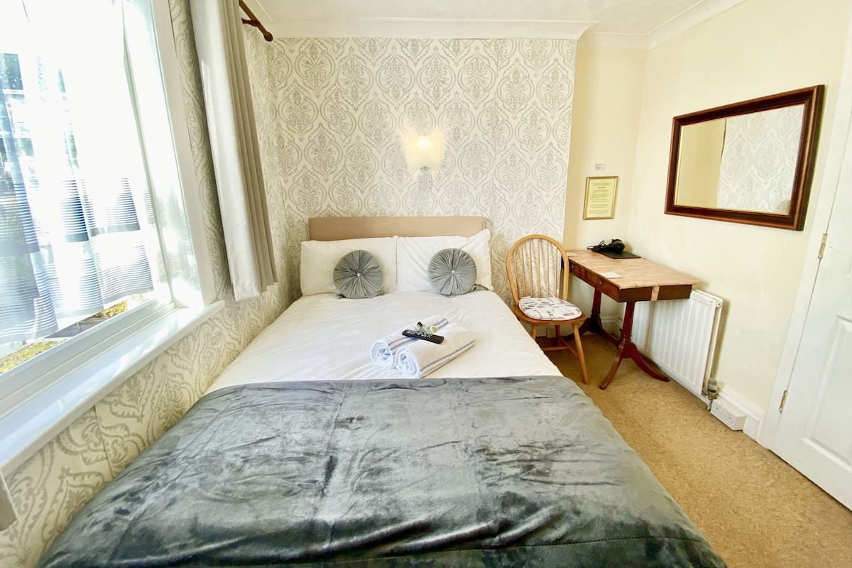 A hotel room with a bed, a desk, a chair, and a large window with curtains.