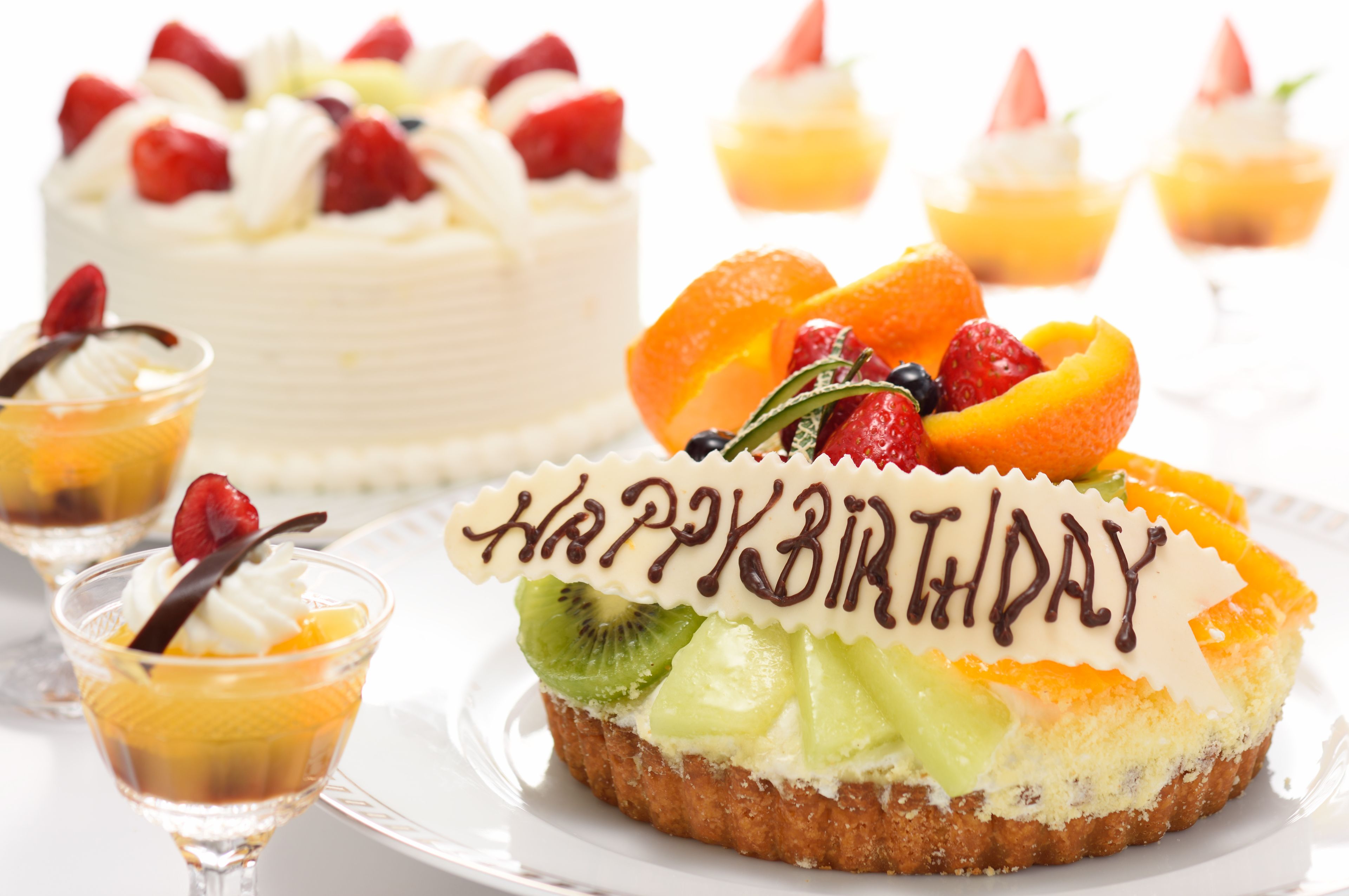 A dessert table with a cake, fruit-topped desserts, and a 'Happy Birthday' sign.