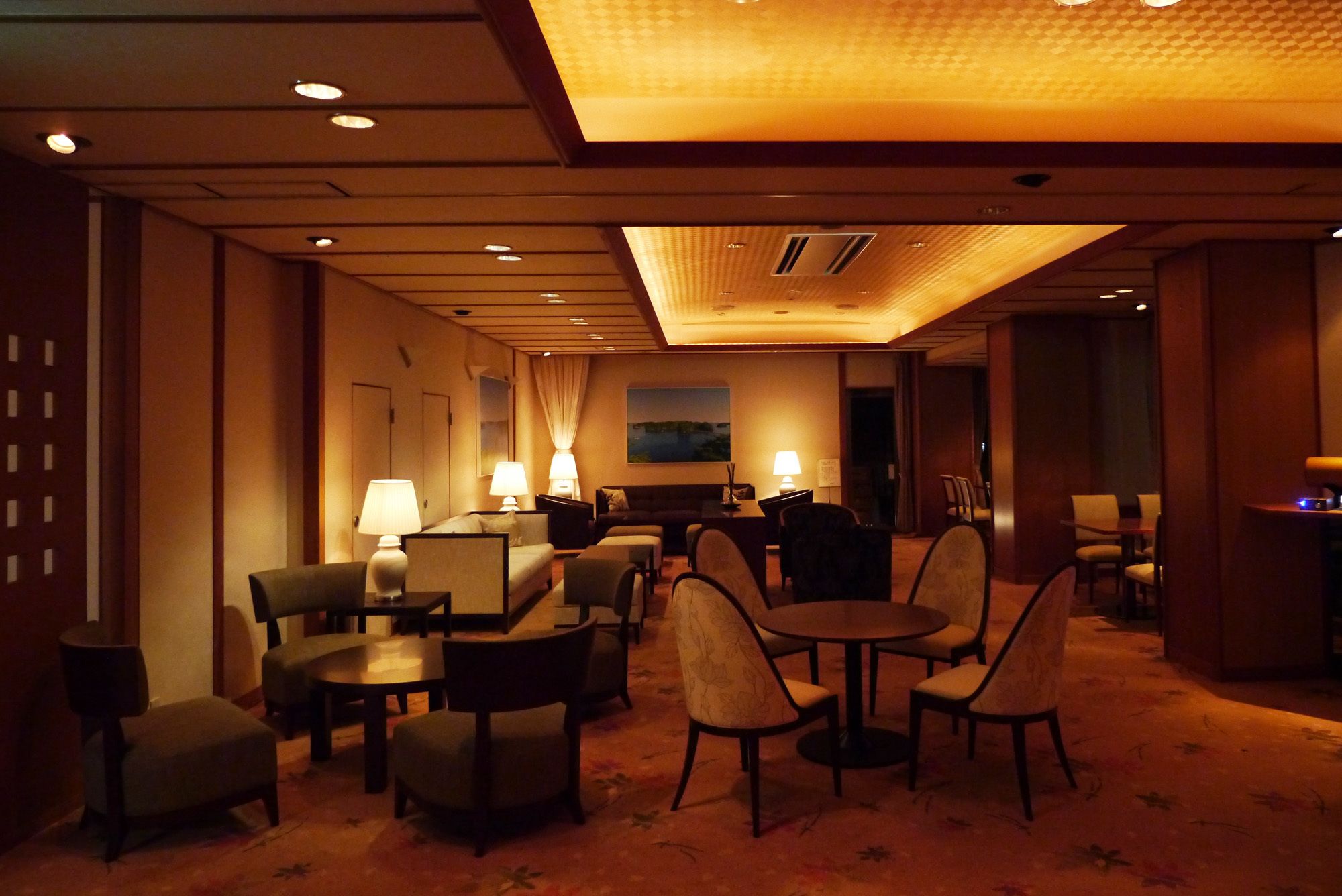 A hotel lobby with a seating area, tables, and lamps.