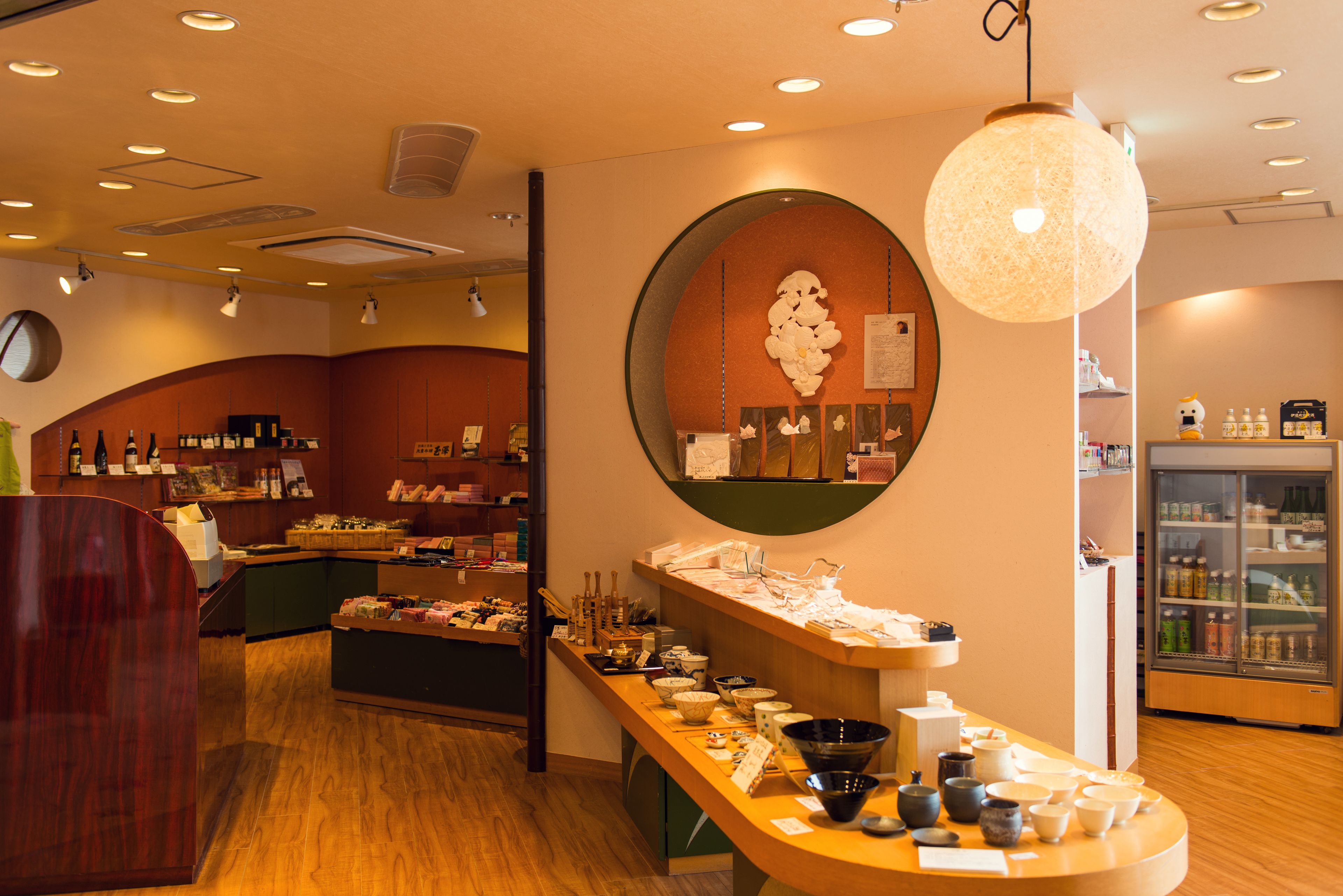 Een restaurantinterieur met een houten toonbank, een decoratieve wand met een ronde spiegel en een koelkast met drankjes.