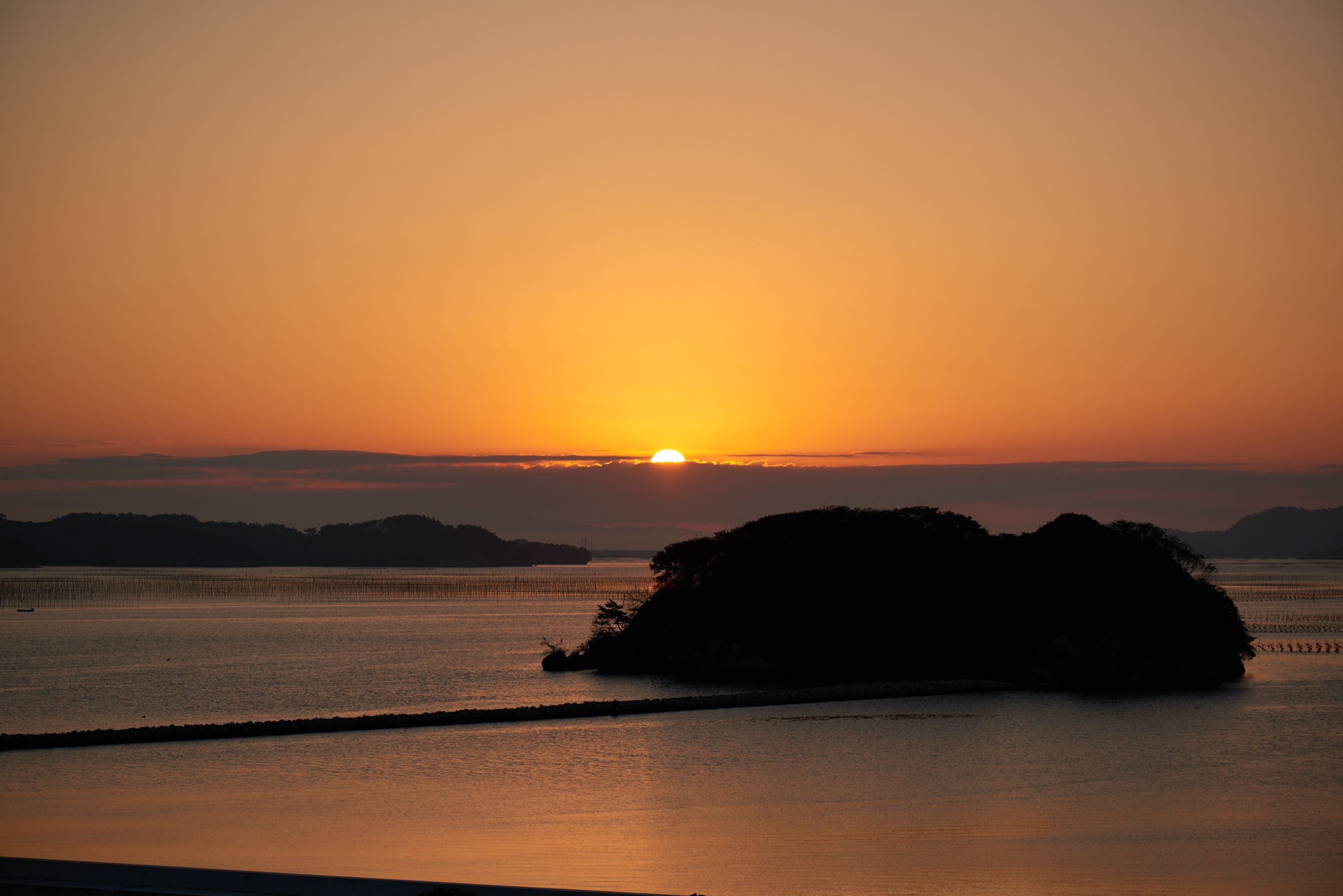 Un coucher de soleil sur une étendue d’eau calme, avec la silhouette d’une petite île.
