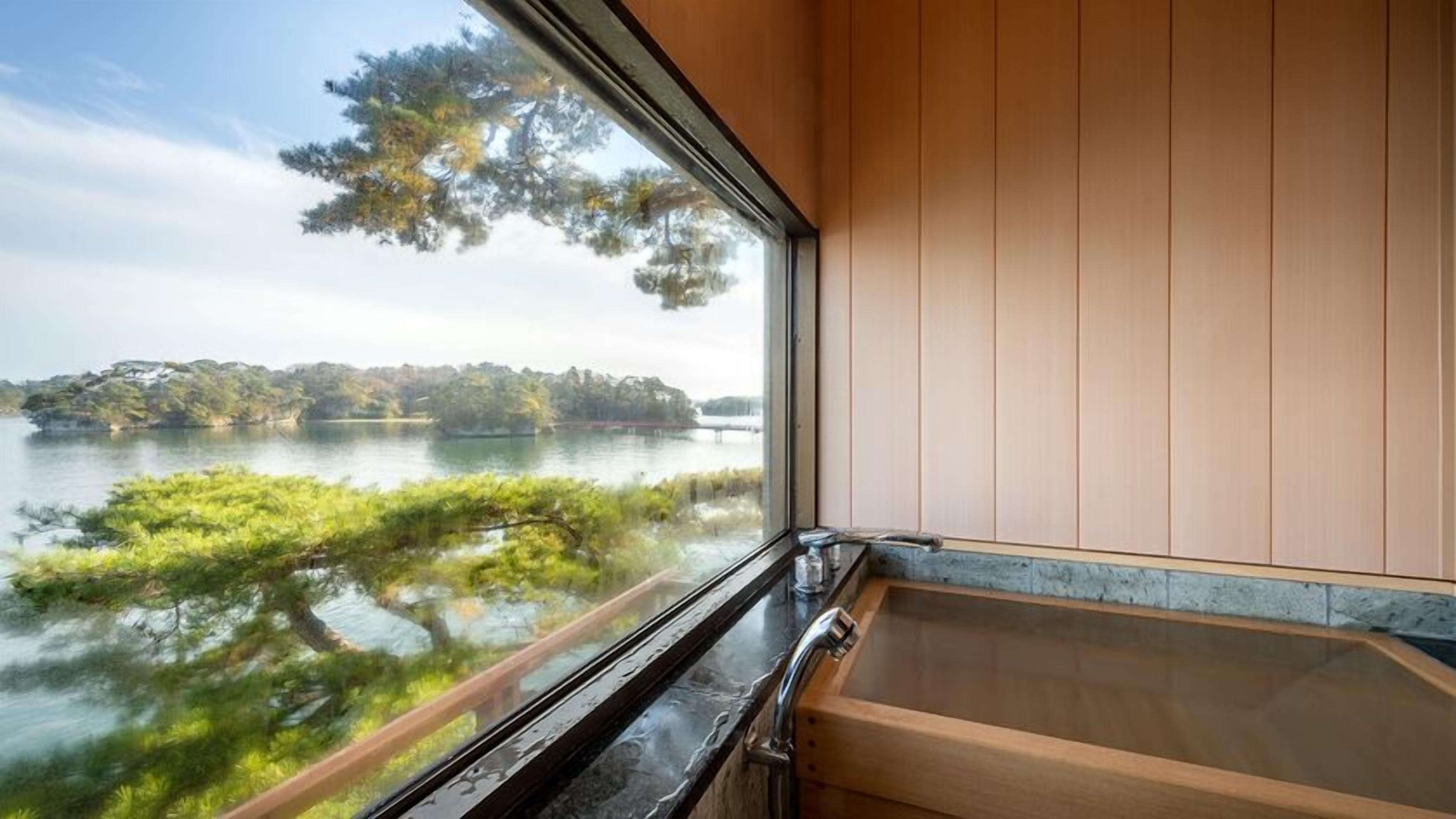 A bathroom with a bathtub, a window overlooking a lake, and a view of trees.
