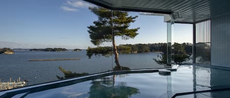 A modern interior with a large glass window overlooking a body of water and a tree.
