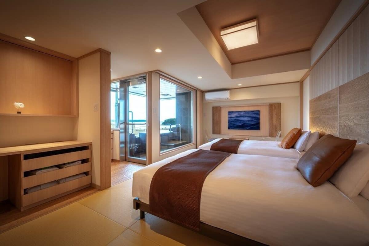 A modern hotel room with a large bed, a seating area, and a view through a glass door.