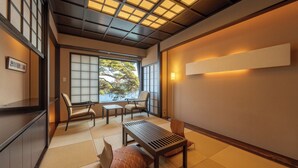 Een traditionele Japanse kamer met tatami vloeren, een lage tafel, stoelen en een schuifdeur met uitzicht op bomen.