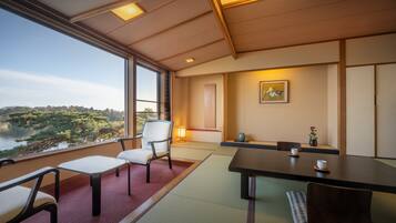 A traditional Japanese-style room with tatami flooring, a low table with cups, and a view of a forested area through large windows.