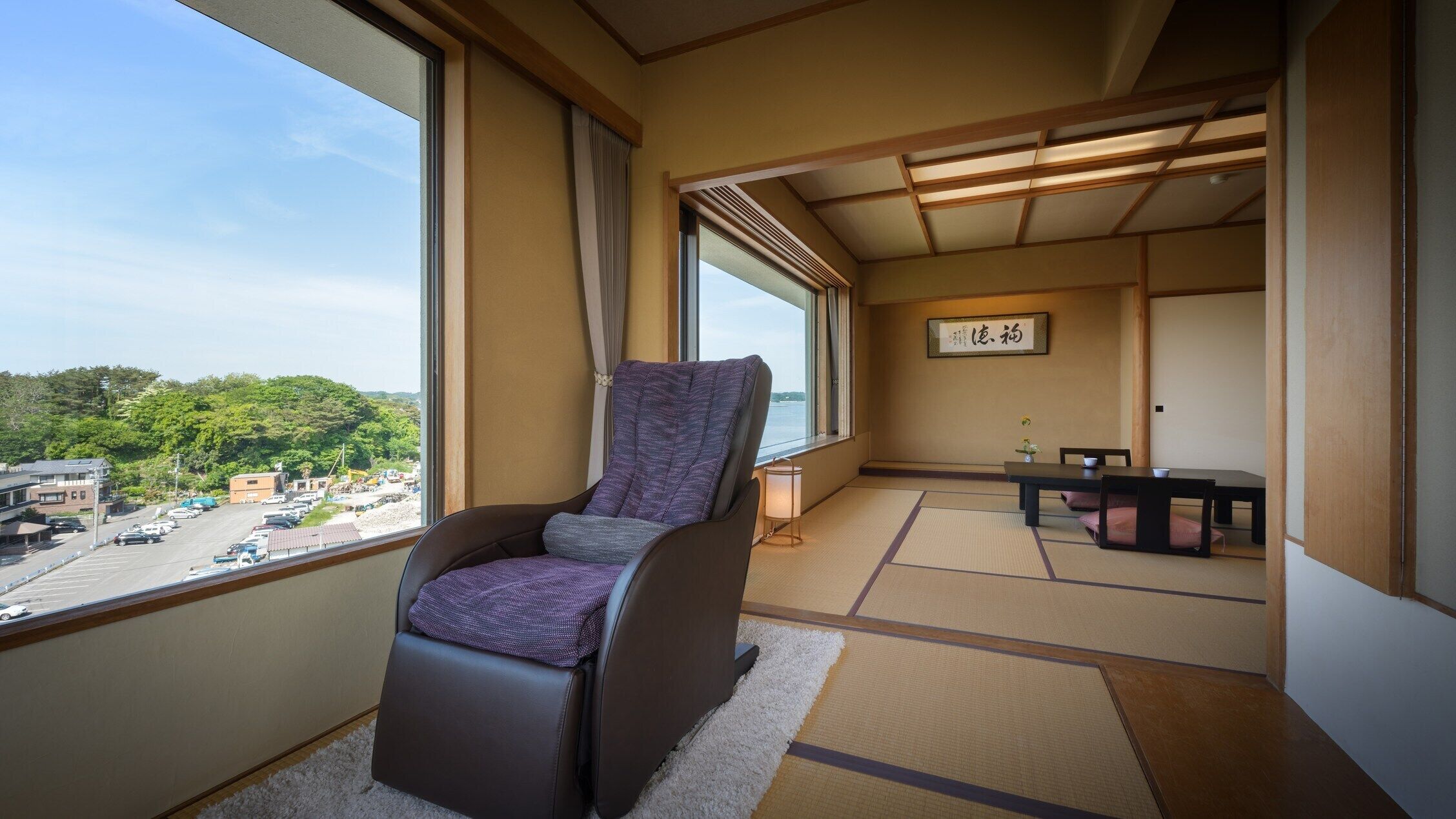 A room with a view of a parking lot and greenery, a tatami mat floor, a traditional Japanese-style chair, and a small table with a tea set.