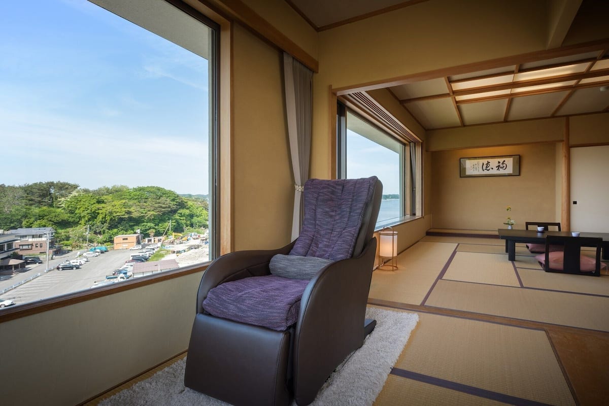 Habitación con vistas a un estacionamiento y áreas verdes, piso de tatami, una silla de estilo japonés tradicional y una pequeña mesa con un juego de té.