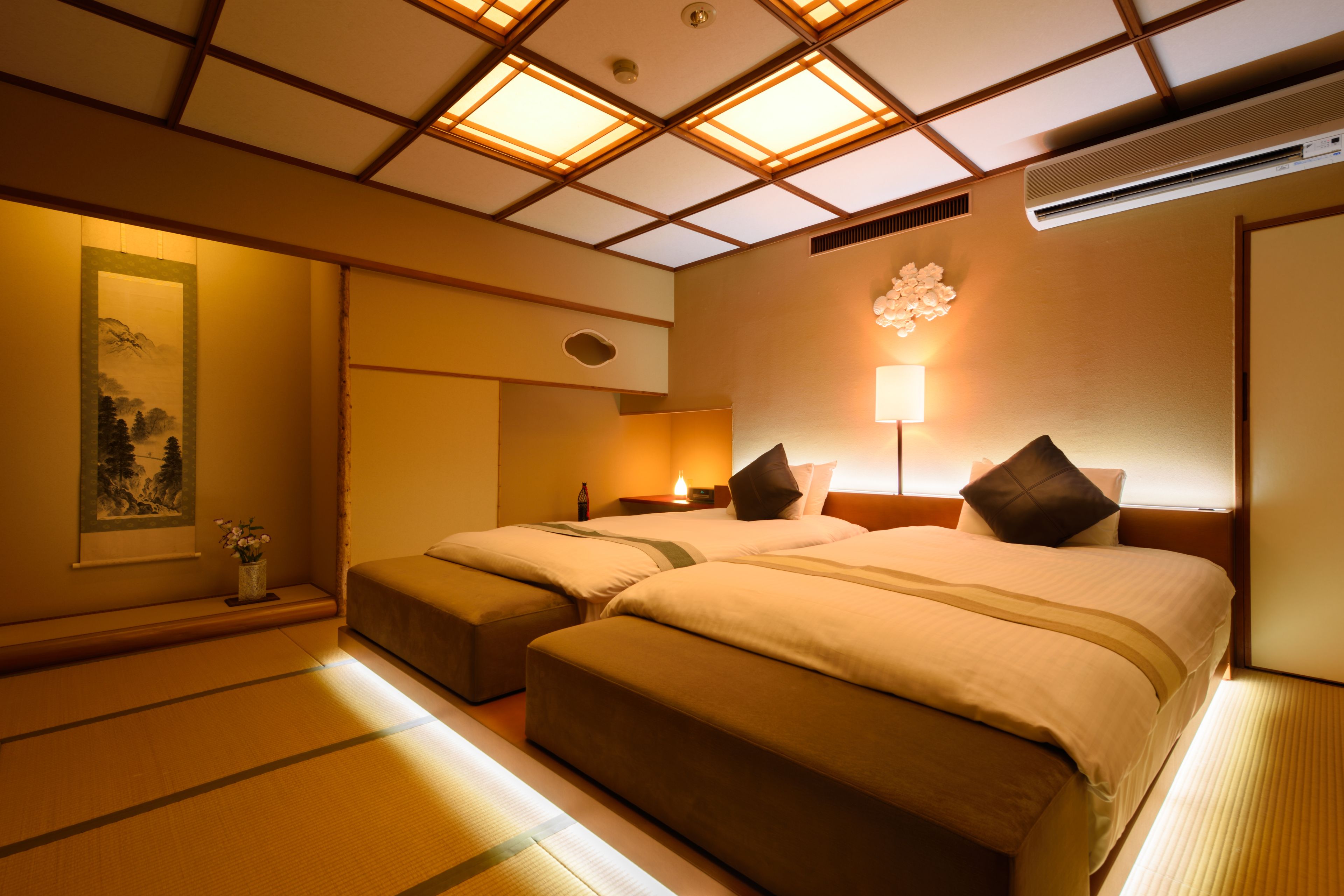 Ein Hotelzimmer mit zwei Betten, einer traditionellen japanischen Decke und einer Wand-Klimaanlage.