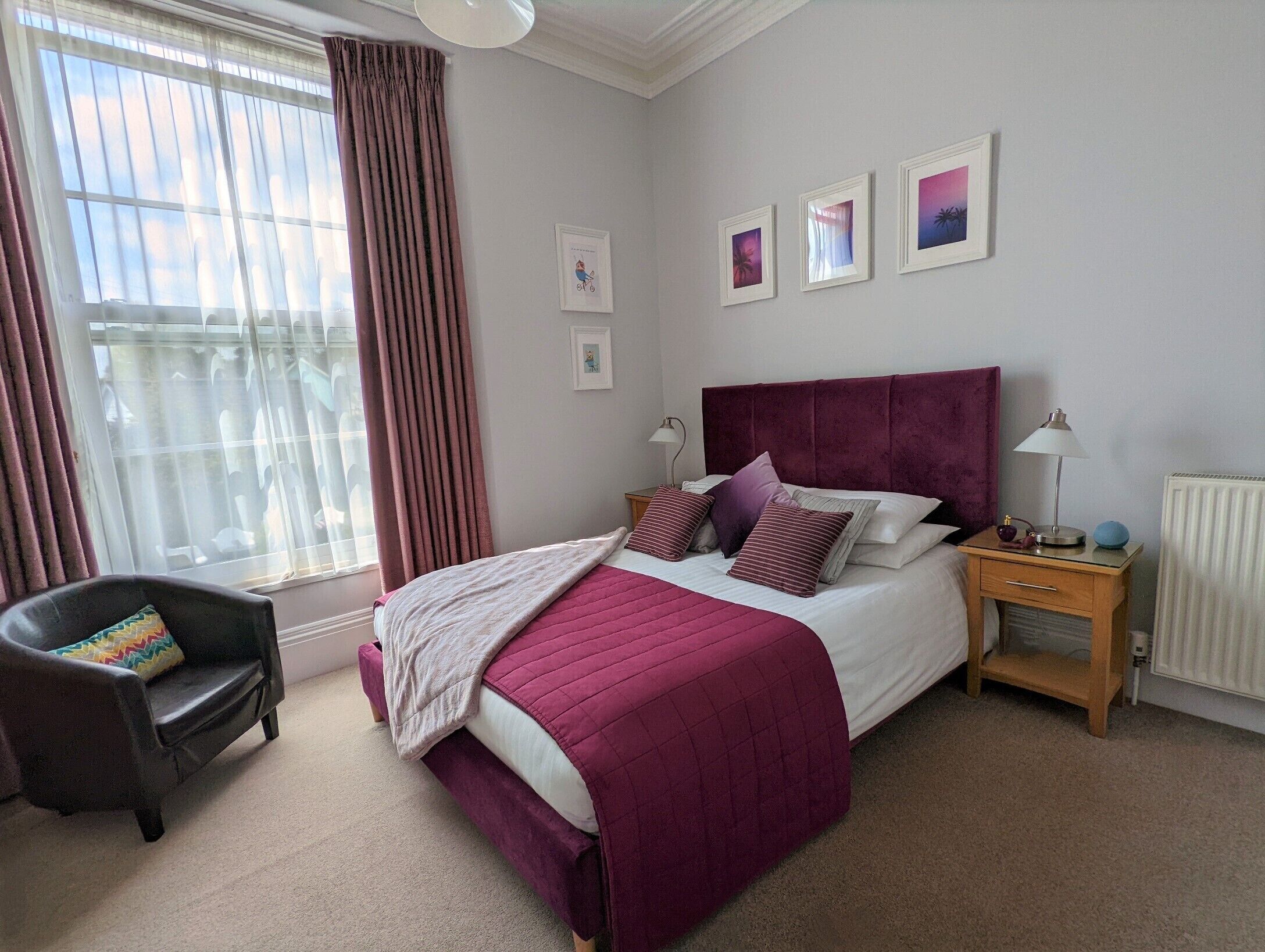 A bedroom with a large bed, a nightstand, a chair, and a window with curtains.