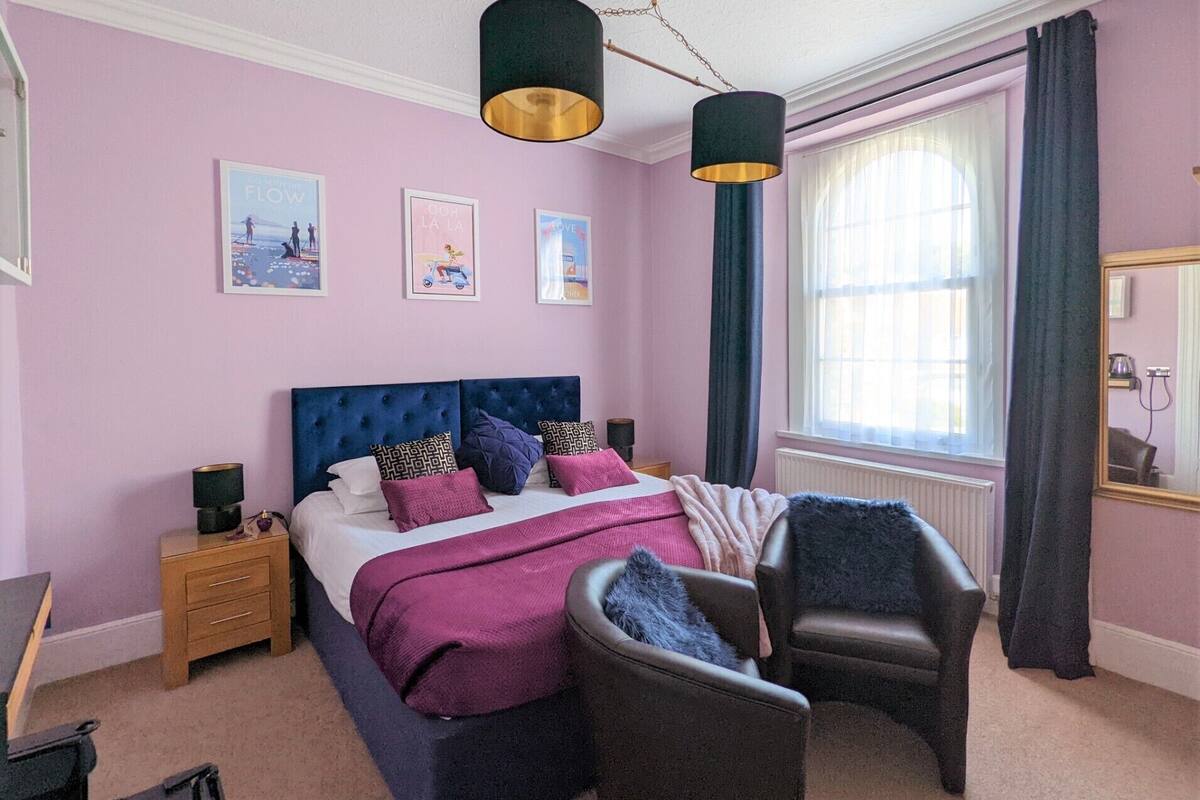 A bedroom with a bed, bedside tables, a chair, a window with curtains, and wall art.