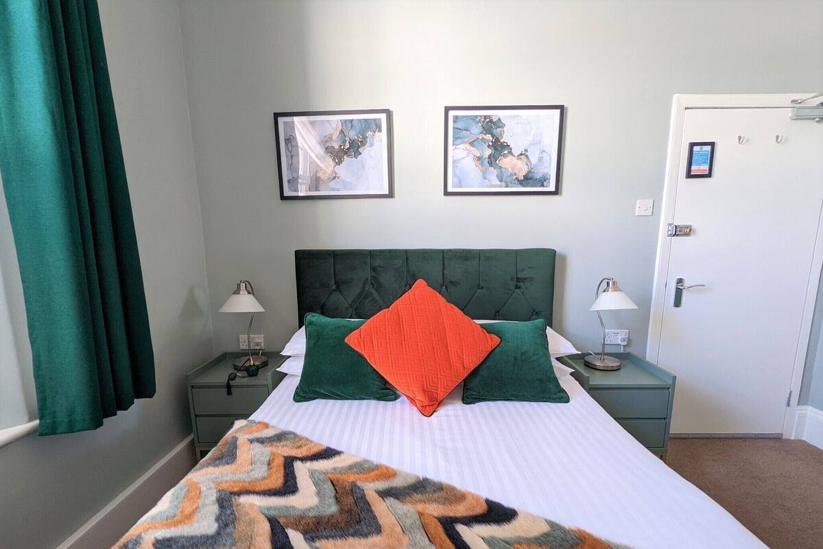A neatly arranged hotel room with a large bed, two bedside tables with lamps, and two framed artworks on the wall.