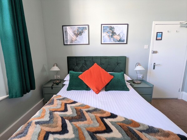 Habitación de hotel ordenada con una cama grande, dos mesitas de noche con lámparas y dos cuadros en la pared.