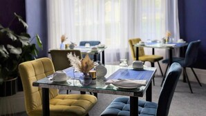 Un comedor con mesas dispuestas para dos, con cubiertas de vidrio y sillas tapizadas en amarillo y azul.