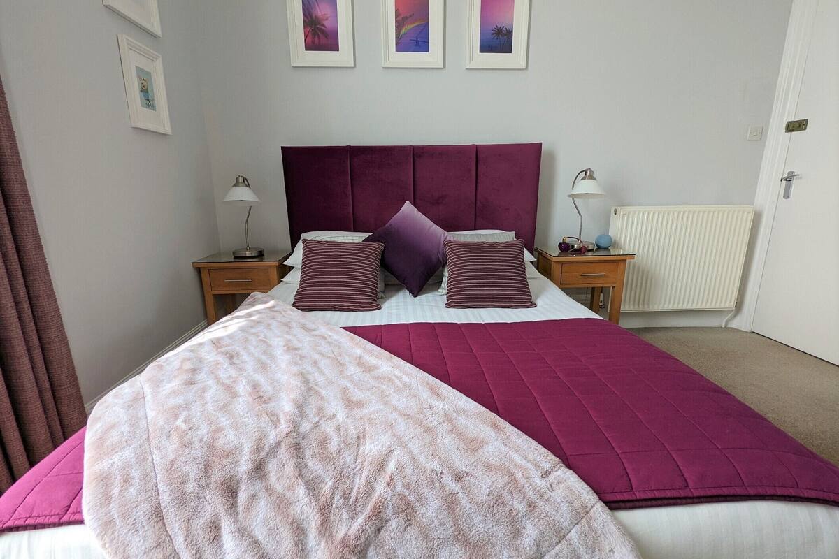 A neatly arranged bedroom with a large bed, two bedside tables, a radiator, and three framed pictures on the wall.