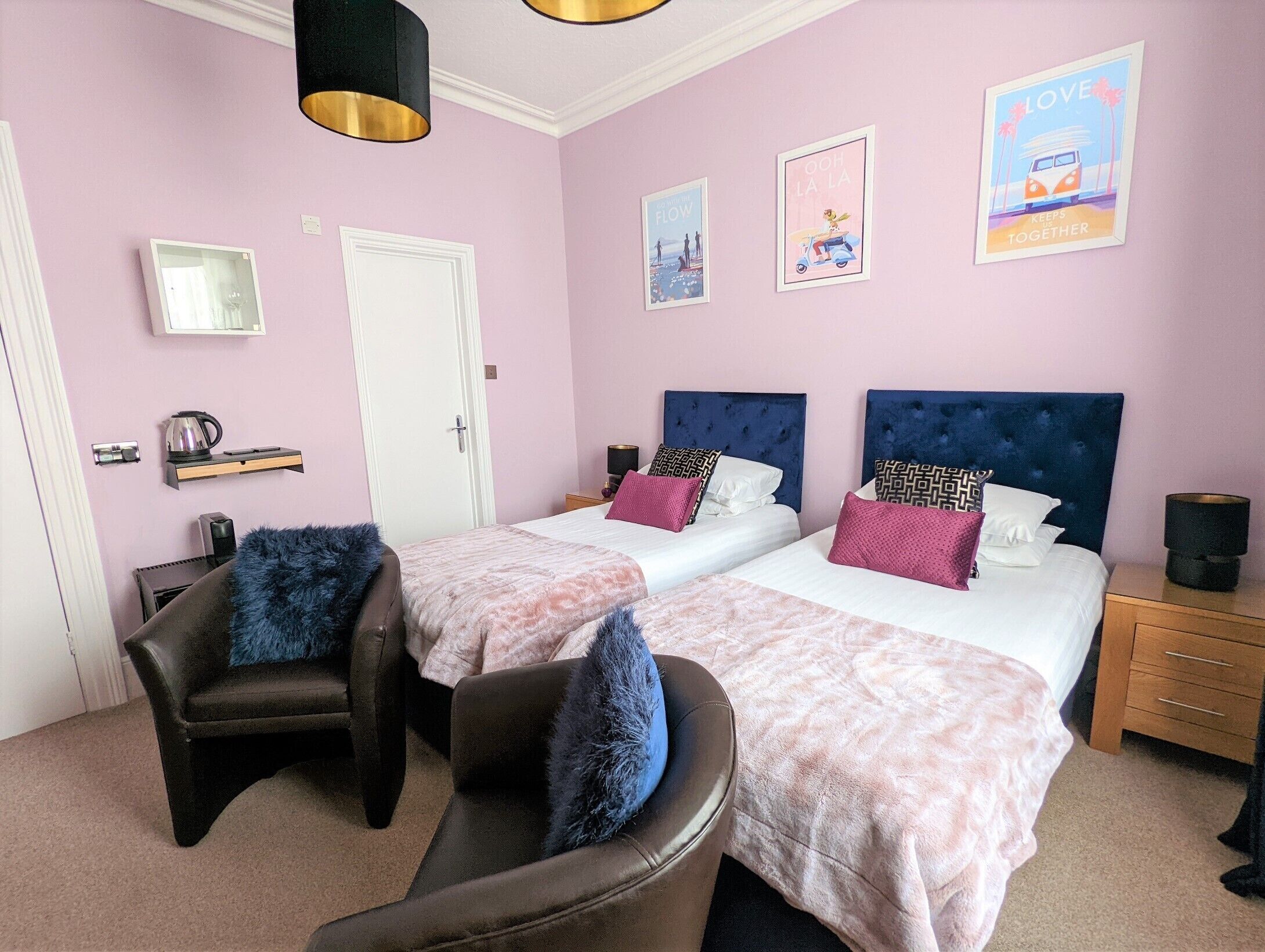 A room with two beds, a chair, a bedside table, a lamp, and a poster on the wall.