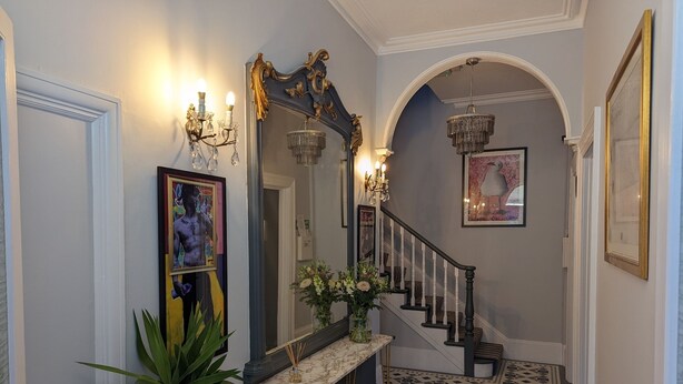 A hallway with a marble console table, a mirror, a staircase with a chandelier, and patterned flooring. - Villa Marina (Torquay)