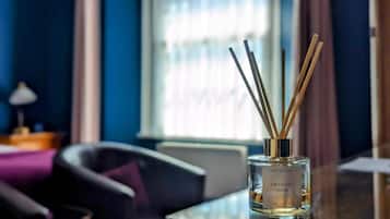 Una bottiglia di colonia Oriental Musk con bastoncini di giunchi su un tavolo in una stanza con una finestra e una sedia.