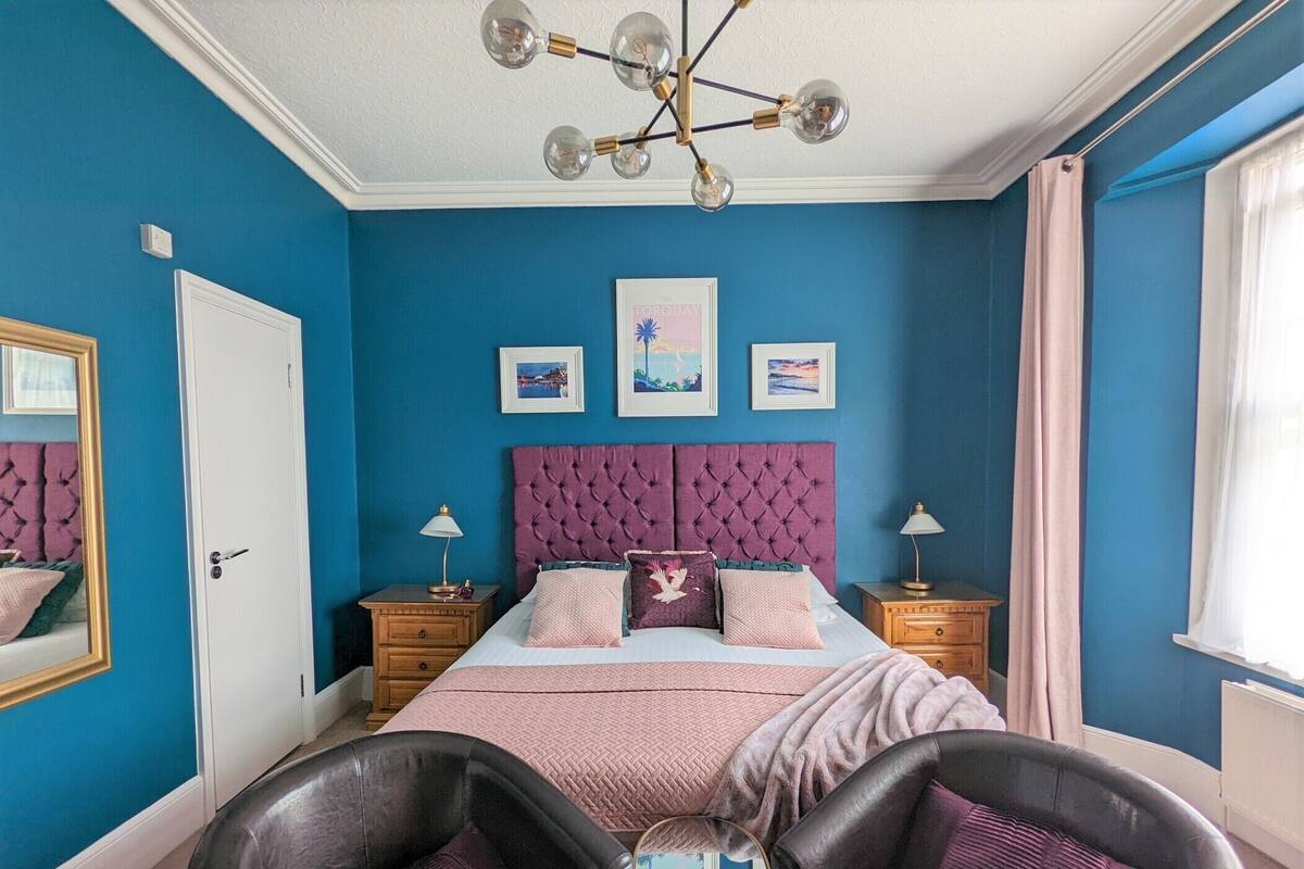 A bedroom with a large bed, two bedside tables, a chandelier, and a window with curtains.