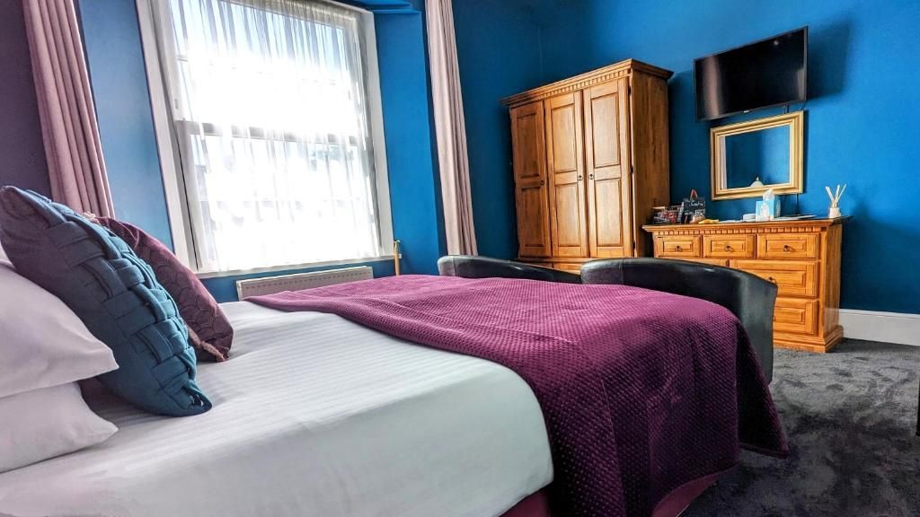 A hotel room with a bed, a desk, a wardrobe, and a television on the wall.