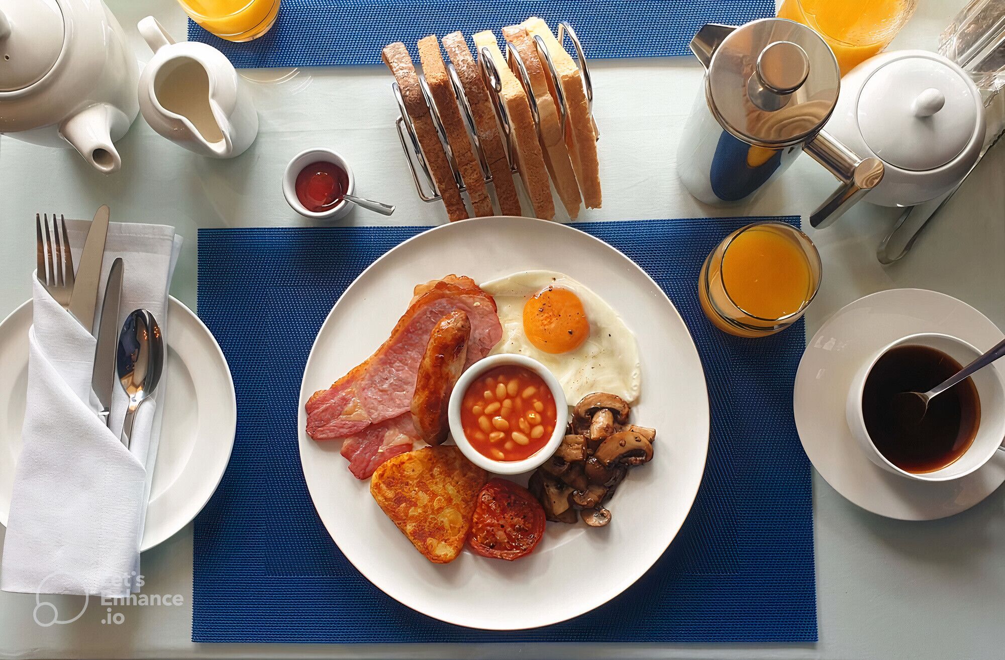 Un desayuno con un plato de huevos, tocino, champiñones, frijoles y tostadas, acompañado de una taza de café y un vaso de jugo de naranja.