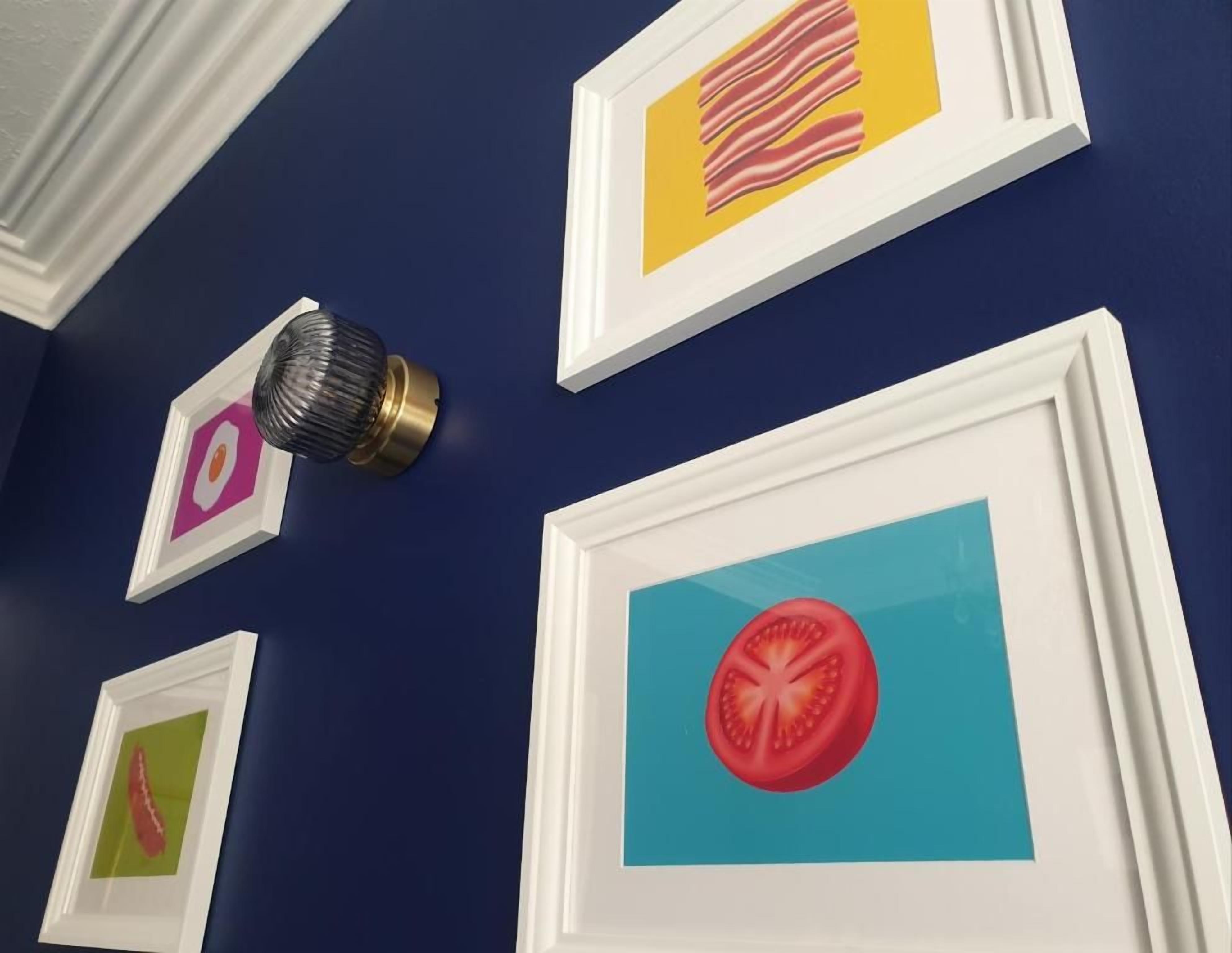 A wall with framed pictures, including a tomato slice and bacon.