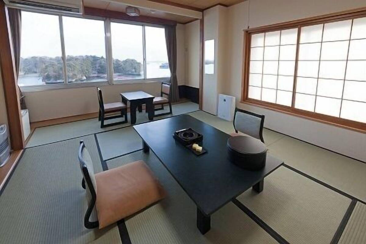 Ein traditioneller japanischer Raum mit Tatami-Böden, einem niedrigen Tisch, Stühlen und Blick auf einen See.